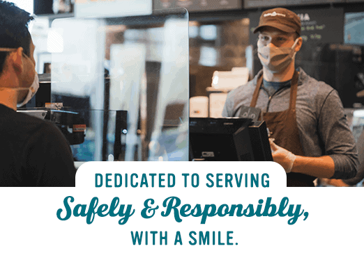 Caribou barista smiling behind plexi shield wearing face covering and gloves while customer orders