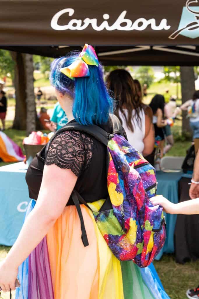 woman with blue hair, rainbow backpack and tutu waiting in line at the caribou coffee tent at the twin cities pride festival