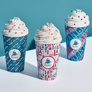 Three Caribou Coffee handcrafted beverages with whipped cream and toppings in festive holiday cups
