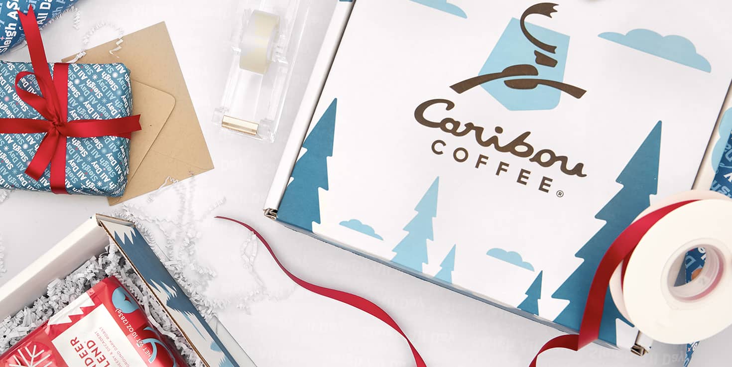 A Caribou Coffee gift box with ribbon, envelopes, wrapping paper and festive items near it