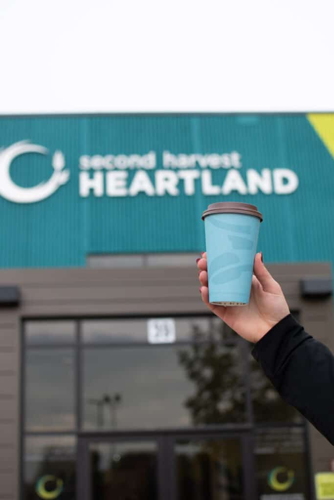 hand holding up a caribou coffee cup in front of second harvest heartland's headquarters