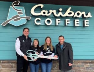 Four people standing under at Caribou Coffee sign holding a giant pair of scissors