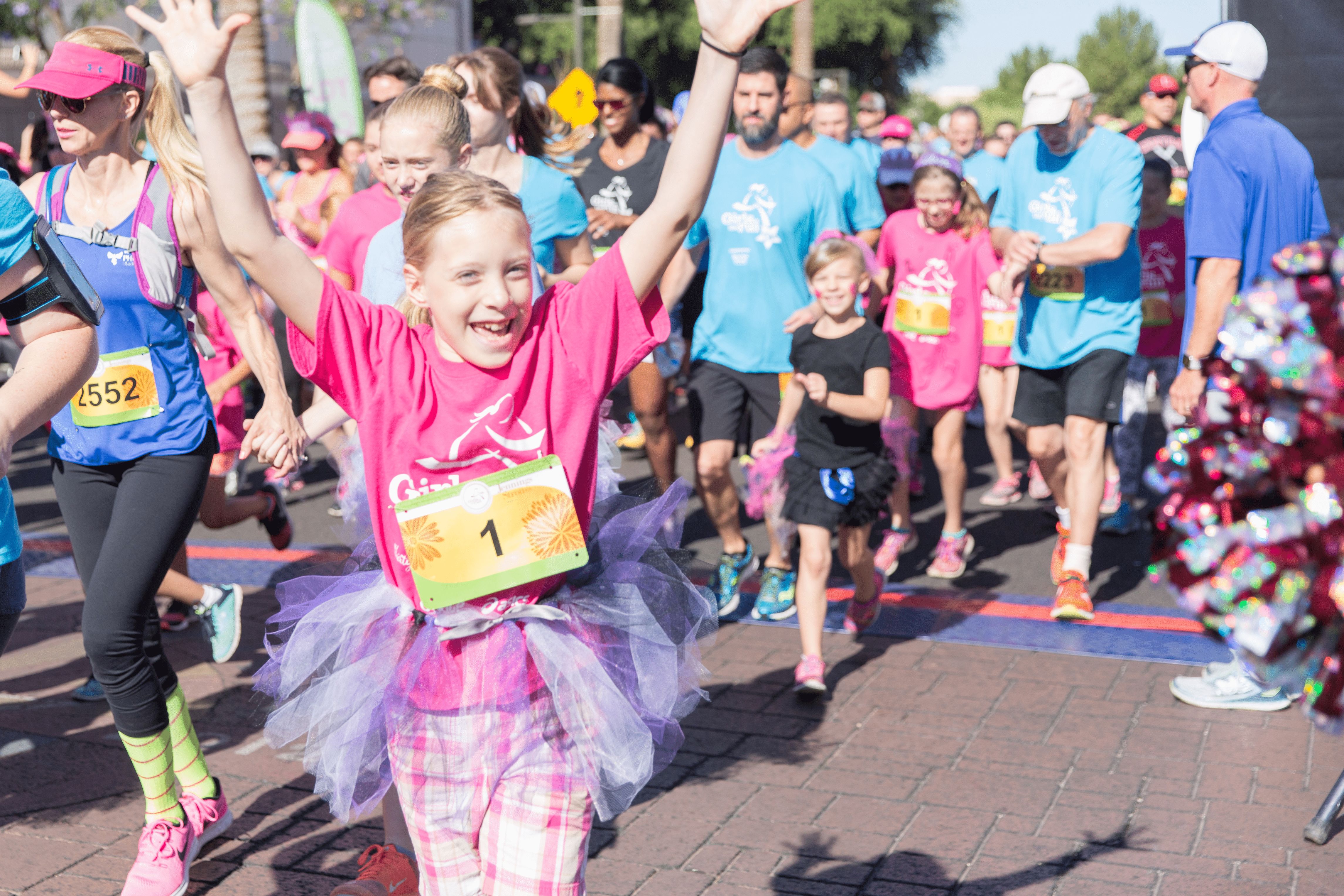 girls on the run participant running through a 5k finish line with hands up in air