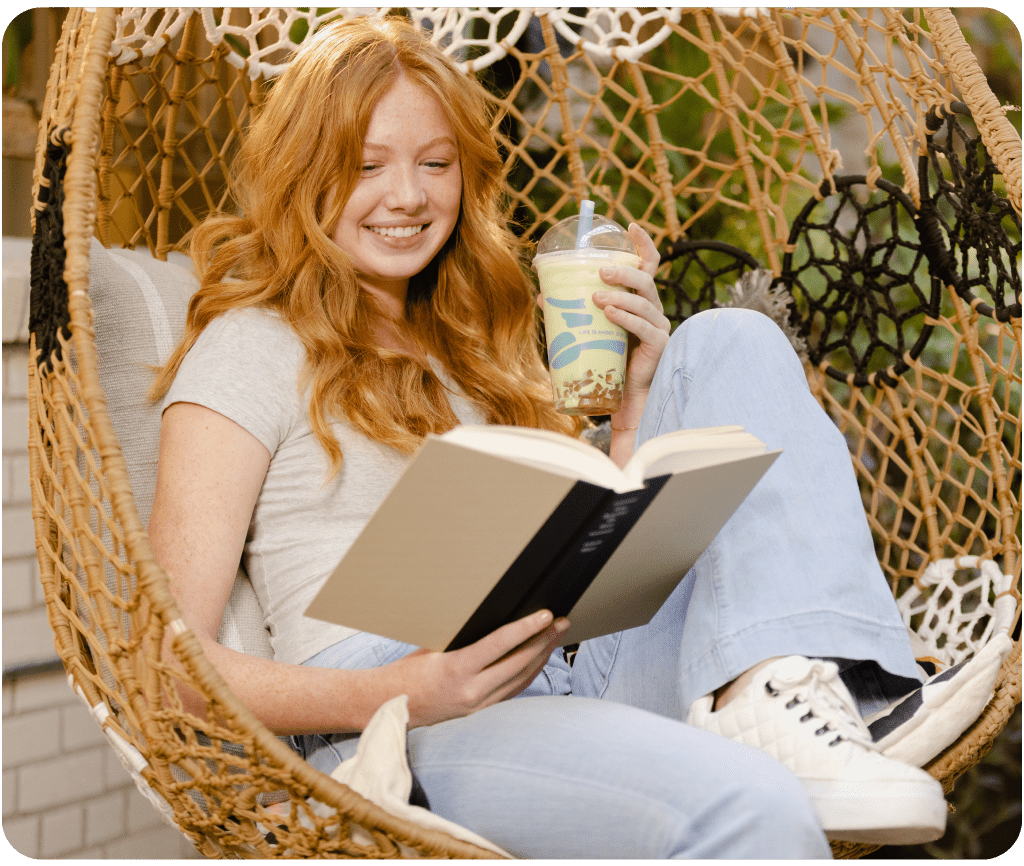 Woman sitting in a chair drinking a Frozen Matcha with Bubbles and reading a book.