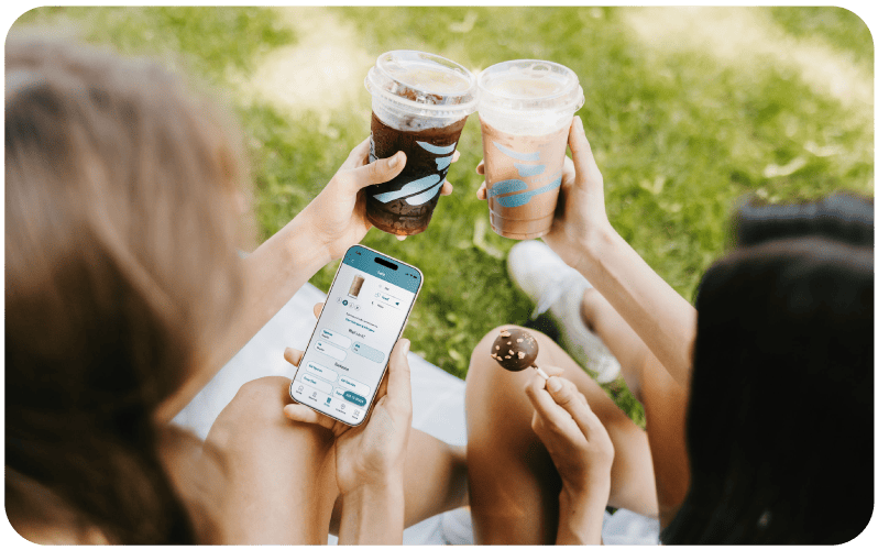 Two people cheersing and looking at the Caribou Coffee app outdoors