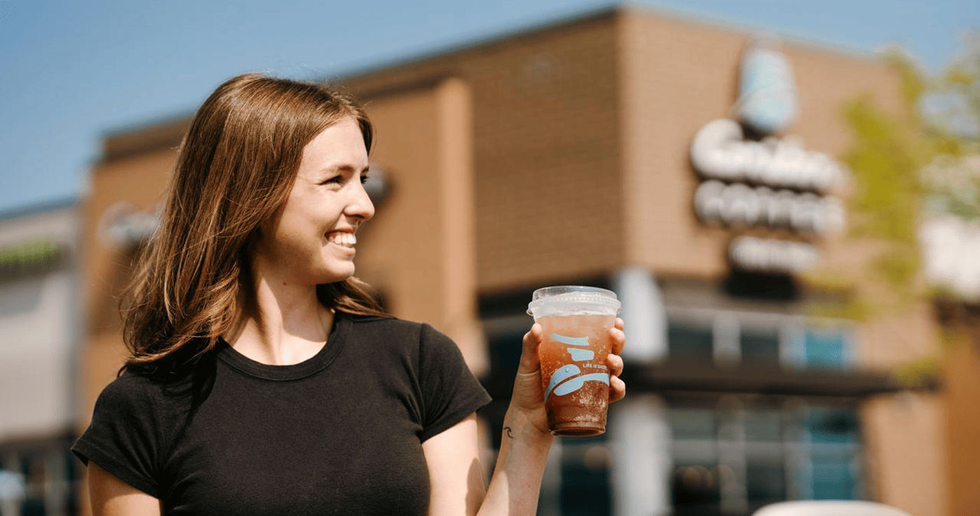 women holding caribou coffee beverage with coffeehouse in background