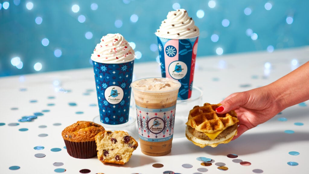 Multiple drinks with holiday and festive wraps on it, a hand holding a waffle breakfast sandwich set to a snowflake background.
