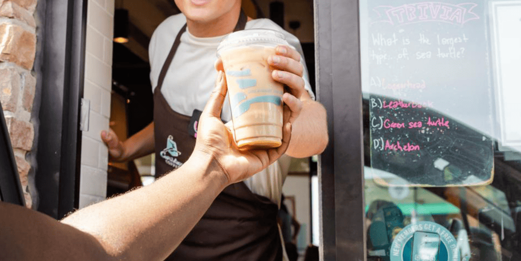 Caribou Coffee BOUrista handing iced coffee beverage out the drive-thru window to a guest